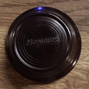 May include: A circular, dark brown knob with a glossy finish and concentric circular ridges. The word Magnavox is embossed in the center of the knob in a stylized, raised font. The object has a smooth, rounded edge and a flat top surface.