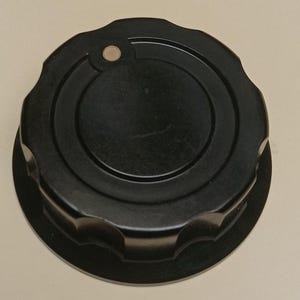 May include: A circular black control knob featuring a scalloped edge and a smooth, flat top surface. A small, circular metallic silver indicator dot is embedded near the outer rim of the knob, providing a clear visual reference point for rotation.