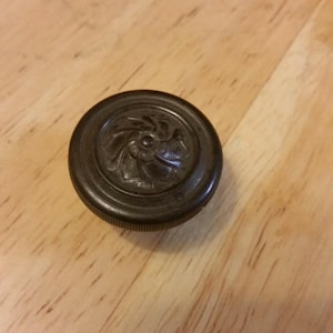 May include: A dark brown, round, plastic bottle stopper with a decorative, swirling design.