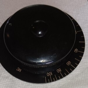 May include: A black, circular control knob with a smaller, raised center. The knob has a dial with white markings and numbers, including "MC" and numbers from 40 to 100. The knob is likely for adjusting a device.