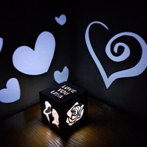 May include: A small wooden box with a light inside casts shadows of hearts on the wall. The box is engraved with the words "Love You Lisa".