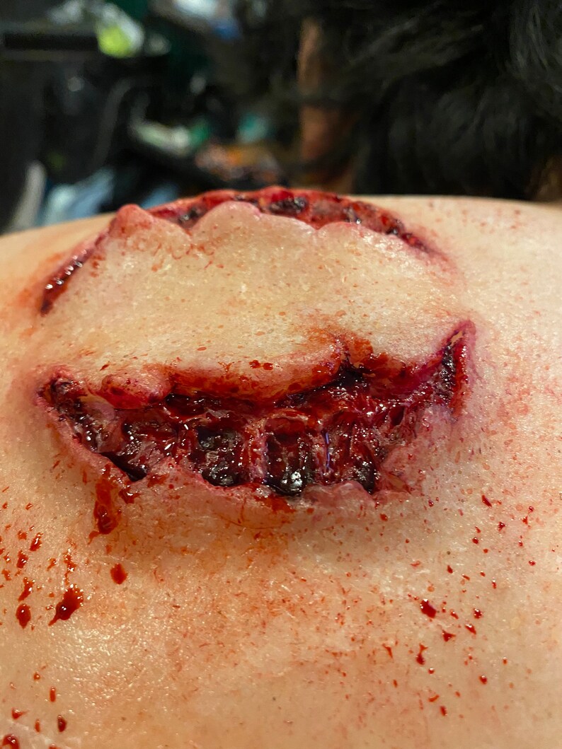 May include: A close-up of a fake, bloody wound on a person's shoulder. The wound is shaped like a mouth with teeth and is dripping blood.