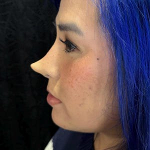 May include: A woman with blue hair is shown in profile. Her face is visible, and she is wearing a dark blue sweater.
