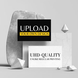 May include: A white card with the text "UHD-QUALITY UNLIKE REGULAR PRINTING" on a grey background. A black card with the text "UPLOAD YOUR OWN DESIGN" is above the white card.