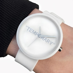 May include: White wristwatch with a round face and a white strap. The watch face displays the word "TEMPORARY" in light grey lettering. The watch is on a wrist.