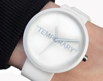 May include: White wristwatch with a round face and a white band. The watch face features the word "TEMPORARY" in light gray lettering. The watch is on a wrist.