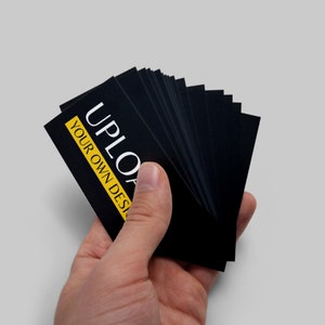 May include: A stack of black business cards with white text that reads "UPLOAD YOUR OWN DESIGN". The text is highlighted with a yellow rectangle.