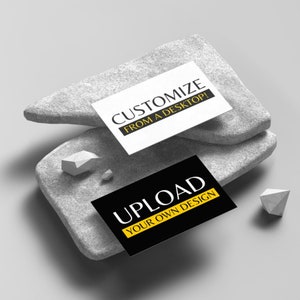 May include: Two business cards on a grey stone surface. The top card is white with black text that reads "Customize from a desktop!" The bottom card is black with white text that reads "Upload your own design" with a yellow stripe.