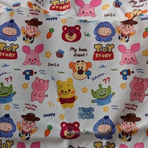 Puede incluir: Tela blanca con un patr&oacute;n repetitivo de personajes de dibujos animados de las pel&iacute;culas de Disney y Pixar. Los personajes incluyen Winnie the Pooh, Piglet, Tigger, Eeyore, personajes de Toy Story, y m&aacute;s. La tela est&aacute; impresa con el texto "Toy Story", "Winnie the Pooh", "&iexcl;Mi mejor amigo!" y "&iexcl;Juguemos juntos!".