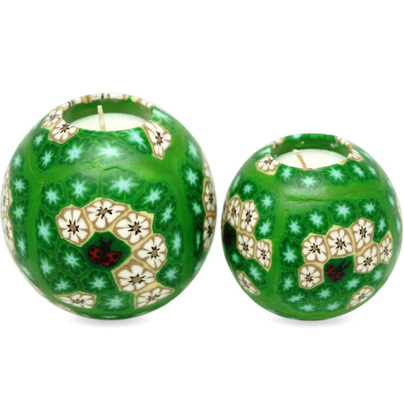 May include: Two green sphere candles with white and brown floral patterns and red ladybugs. The candles are made of a textured material and have a white wax centre.
