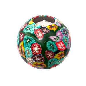 May include: A green round candle holder with a floral design. The holder has a white candle inside.