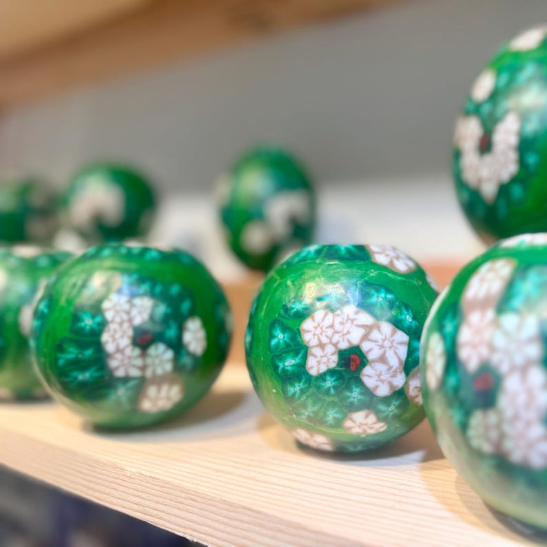 May include: A collection of green and white patterned ornaments with floral designs. The ornaments are round and have a glossy finish.