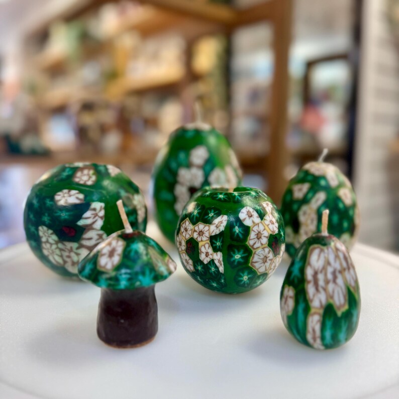 May include: A set of six green and white candles with floral designs. The candles are shaped like spheres and a mushroom.