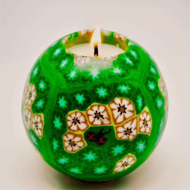 A handcrafted spherical candle with a vibrant green base, featuring intricate floral patterns and a small ladybug design. This unique, decorative candle adds a touch of elegance and charm to any space, perfect for home décor or as a thoughtful gift.