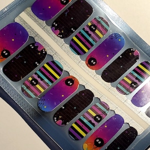 May include: A sheet of nail wraps with a Halloween theme. The wraps feature black cats, spiders, and stripes in a variety of colors, including purple, pink, yellow, and black.