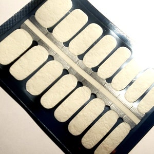 May include: A sheet of white nail polish wraps with a delicate floral pattern. The wraps are packaged in a blue plastic sleeve.