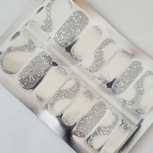 May include: A sheet of white nail polish wraps with silver glitter. The wraps are packaged in a silver foil pouch.