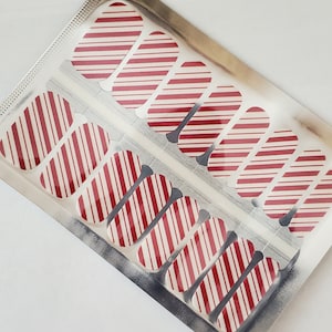May include: A sheet of red and white striped nail wraps in a silver foil package. The nail wraps are designed to look like candy canes.