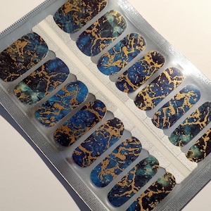 May include: A set of nail wraps with a blue and gold marble design. The wraps are packaged in a clear plastic pouch.