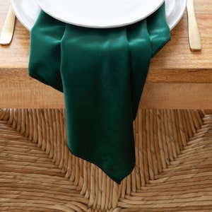 May include: A white dinner plate with a smaller white plate on top, both plates are on a green velvet napkin. The napkin is folded in a triangle shape and is on a wooden table.