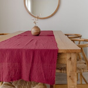 May include: A wooden dining table with a red runner and two chairs. A round wooden mirror hangs on the wall above the table. A small wooden vase with dried flowers sits on the table.