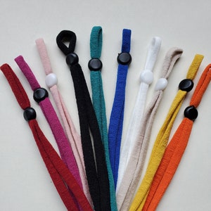 May include: Ten colourful fabric mask extenders with adjustable toggles. The extenders are in red, pink, black, teal, blue, beige, yellow, and orange.
