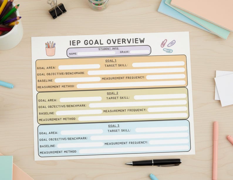 May include: A printed IEP Goal Overview sheet with sections for student information and three goals. The sheet includes areas for goal objectives, baselines, and measurement methods. A pencil holder, paperclips, pens, and a black pen are also visible.