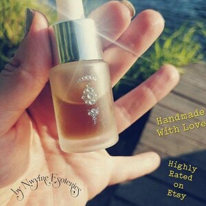 May include: A clear glass bottle with a silver cap and a decorative design of rhinestones. The bottle is filled with a light brown liquid. The text "Handmade with Love" and "Highly Rated on Etsy" is visible in the background.