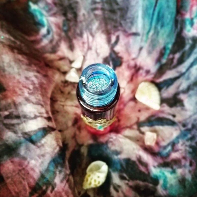 May include: A small glass bottle with a blue top and a gold band around the middle. The bottle is filled with a glittery blue liquid.