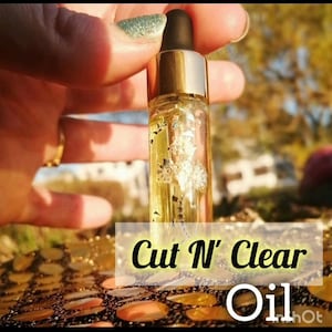 May include: A small glass bottle with a gold cap and a black dropper, filled with a clear, yellow liquid containing decorative elements. The bottle is labeled "Cut N' Clear Oil".