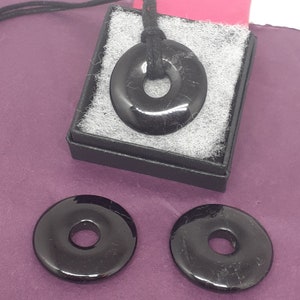 May include: Three black obsidian donut pendants, one on a black cord in a black box, and two loose. The pendants are smooth and shiny.