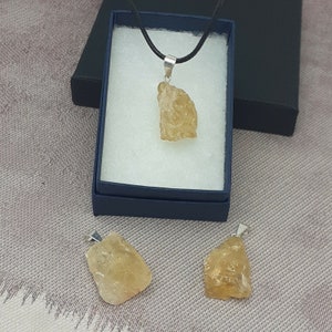 May include: Three raw, natural, yellow citrine crystal pendants on silver chains. The pendants are different sizes and shapes. The pendants are on a white background.