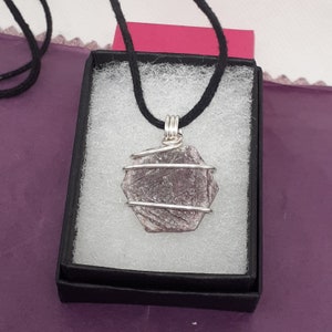 May include: A silver necklace with a wire-wrapped purple gemstone pendant. The pendant is a hexagonal shape and has a natural, rough texture.