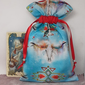 May include: A blue and red drawstring bag with a white skull design and a silver charm. The bag has a geometric pattern at the bottom and is made of fabric.