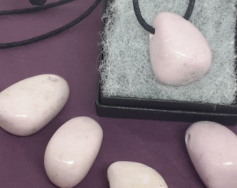May include: Five smooth, pale pink, oval-shaped stones. One stone is on a black cord necklace, and the other four stones are on a purple surface.