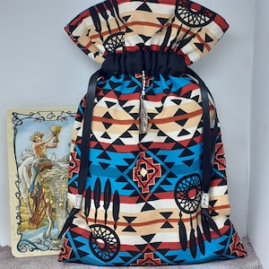 May include: A drawstring bag with a Native American inspired design. The bag is made of fabric with a black, red, blue, and white geometric pattern. The bag has a black drawstring and a silver charm.