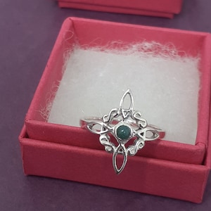 May include: A silver ring with a green gemstone set in a Celtic knot design. The ring is in a red jewelry box.