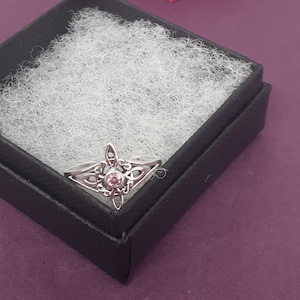 May include: A silver ring with a pink gemstone set in a Celtic knot design.