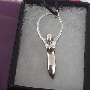 May include: Silver pendant necklace featuring a stylized female figure with arms raised, holding a circle above her head.