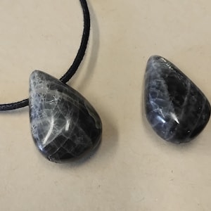 以下が含まれることがあります： 黒い紐に、黒と白の涙滴型のペンダントが2つ。ペンダントはマーブル模様です。