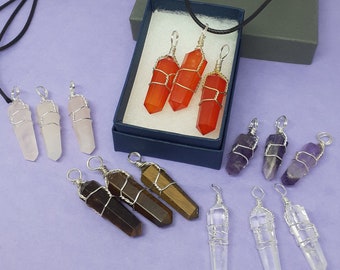May include: A collection of 10 crystal point pendants with silver wire wrapping. The pendants are in various colors, including red, pink, purple, and clear. The pendants are displayed on a light purple surface.