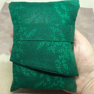 May include: A green fabric pouch with a leafy pattern. The pouch is folded in half and has a seam down the centre.