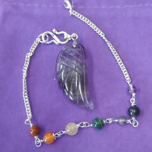 May include: A silver chain bracelet with a carved amethyst wing pendant and various colored gemstone beads. The beads include amethyst, red jasper, carnelian, clear quartz, green aventurine, and black onyx.