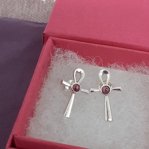 Puede incluir: Un par de pendientes de plata con una piedra rosa en el centro de cada pendiente. Los pendientes tienen forma de ankh, un antiguo símbolo egipcio de la vida.