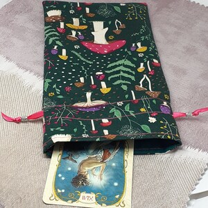 May include: A green fabric pouch with a pink drawstring and a white card inside. The pouch features a repeating pattern of mushrooms and flowers. The card has a picture of a woman with wings and the text "XIV" on it.