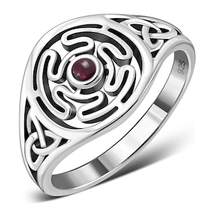 May include: A silver ring featuring a Celtic knot design and a red gemstone at its centre. The ring is marked "925" on the side.