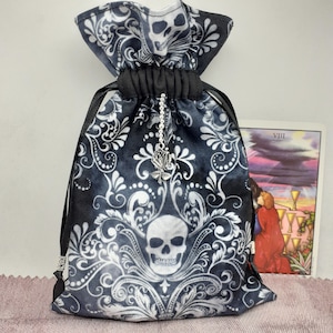 May include: Black velvet drawstring bag with a white damask pattern and a silver skull charm. The bag is decorated with a silver rose and a silver skull.
