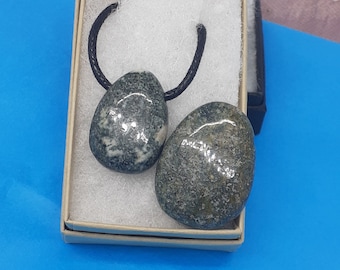 May include: A black cord necklace with two grey and black stone pendants. The stones are oval shaped and have a speckled pattern.