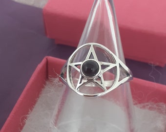 Puede incluir: Un anillo de plata con una piedra preciosa negra en el centro de un diseño de estrella de cinco puntas.