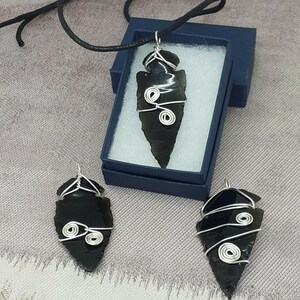 May include: Three black arrowhead pendants with silver wire wrapped around them. The arrowheads are in different sizes and have a smooth, polished finish.